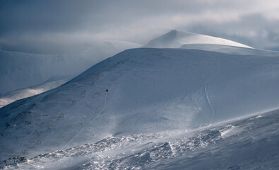 Snow covered mountain slope in last evening sunlight. Magnificent windy dusk on tops above...