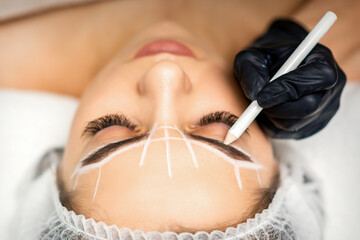 The beautician marks the eyebrow with a white pencil to prepare a permanent makeup procedure
