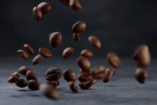 Grains of roasted coffee falling on gray stone background. Levitation coffee beans. Shallow depth of field	
