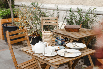 street cafe without people with dirty white dishes on wooden table with cutlery