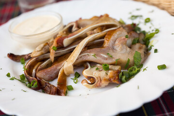 delicious smoked pork ears served with sour cream and herbs on a white plate in a restaurant