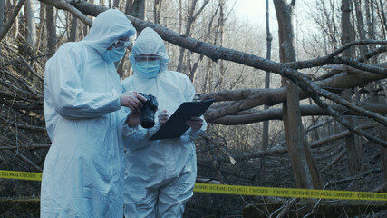 Detectives are collecting evidence in a crime scene. Forensic specialists are making expertise. Police investigation in a forest.