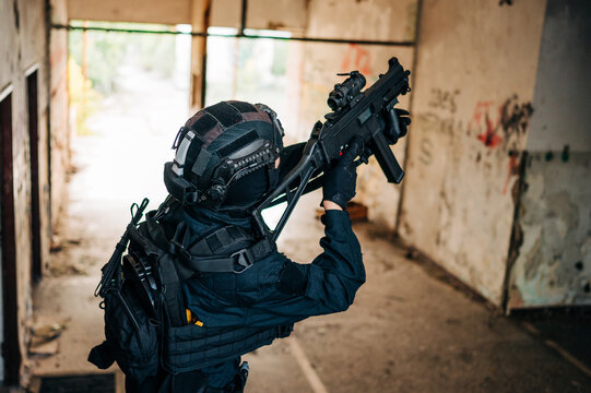 Woman as a police member of swat unit wearing a black jumpsuit and carrying UMP assault rifle. Photos in the abandoned building.