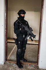Woman as a police member of swat unit wearing a black jumpsuit and carrying UMP assault rifle. Photos in the abandoned building. - obrazy, fototapety, plakaty