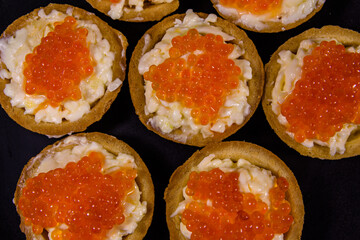 Tartlets with red caviar on a black plate. Festive food. Top view