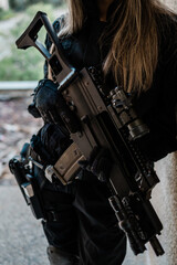 Woman as a police member of swat unit wearing a black jumpsuit and carrying UMP assault rifle. Photos in the abandoned building.