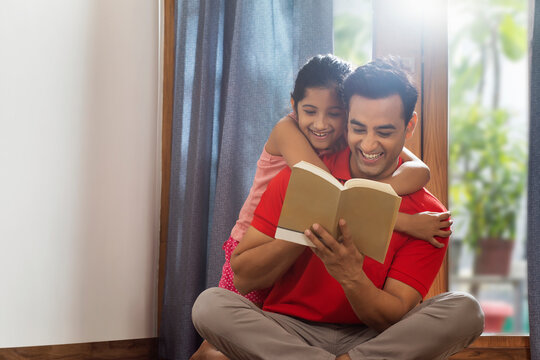 Father and daughter reading a book on the floor	 