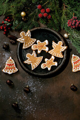 Homemade traditional Christmas gingerbread cookies with icing ornate. Gingerbread Man, angel, bell on ceramic plate with xmas decorations over dark background. Flat lay