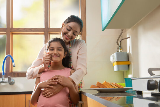 mother affectionately pulls the daughters cheeks in the kitchen	