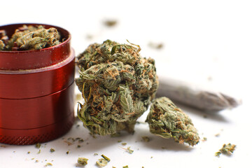 Cannabis branch, joint and red grinder isolated in a white background. Marijuana legalization. Medical cannabis. Drug addiction.