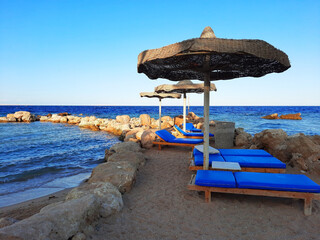 Blue sun loungers under umbrellas on a rocky beach by the sea