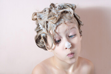 a little blonde girl washes her hair in the shower with foam on her hair and nose. playing in the bathroom with foam