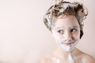 a little girl plays in the bathroom with her face smeared with shampoo foam