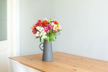 Colorful flowers in a cement vase on a wooden table in grey room with copyspace