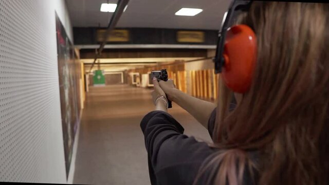 Long haired woman in protective headphones trainings in shooting range, targeting