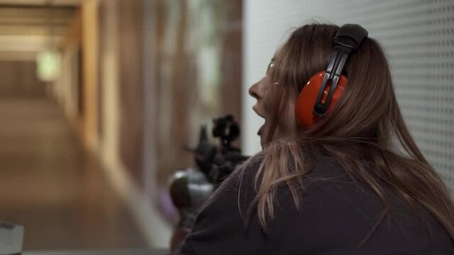 Woman with rifle in hands at shooting range with target, excited and surprised