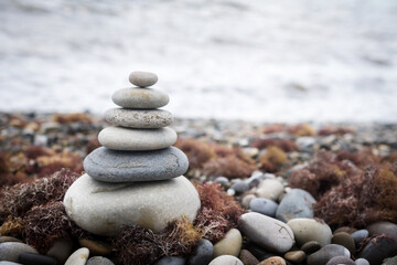 pyramid of stones on the beach against the background of sea waves, stone beach and seaweed
