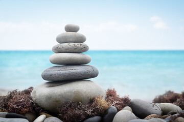 pyramid of stones on the beach against the background of sea waves, blue sky, stone beach and seaweed