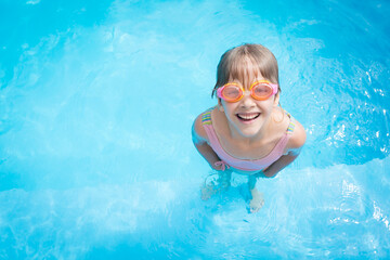 a little girl in a bathing suit and pink swimming glasses swims in a pool with blue water