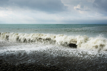 Fototapeta na wymiar Seascape. Waves roll on the shore against the background of a pre-storm sky with clouds. Water of different colors, white foam.