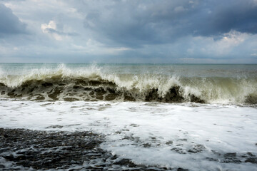 Seascape. Waves roll on the shore against the background of a pre-storm sky with clouds. Water of different colors, white foam.
