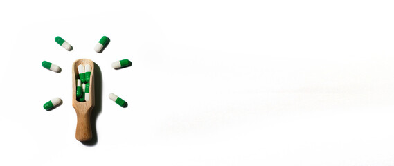 medicine green pills on white background on a wooden spoon in the form of a light bulb . Copy space for text. banner