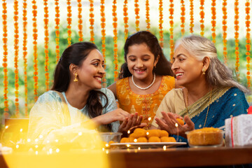 Mother in law teaching daughter in law how to make Ladoo on the occasion of Diwali as the grand daughter looks on	