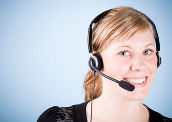 Blonde smiling girl with headset. Studio photo isolated on light blue background.