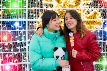 Young teenagers having fun together in christmas date. Happy young friends with a teddy bear and sweet candy in their hands. Travel, love and friendship concept. Focus on face girl