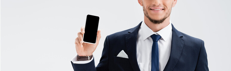 cropped view of young businessman in suit presenting smartphone isolated on white, banner