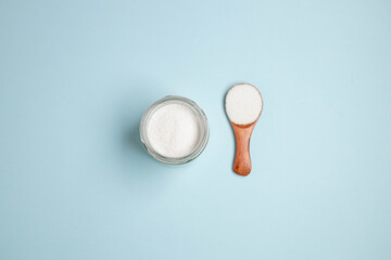 Top view of collagen powder or protein in a glass bowl and small wooden spoon on beige coral background with copy space. Healthy lifestyle concept.