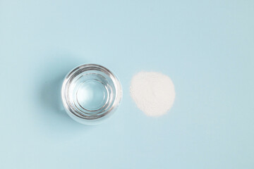 Collagen powder and glass of water on a blue background. Horizontal minimal banner.