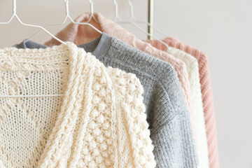 Bunch of knitted warm pastel color sweaters with different vertical knitting patterns hanging on...
