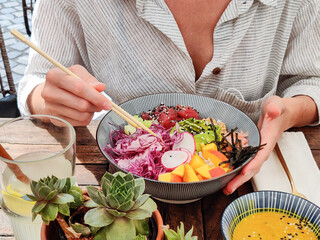 Woman eating tasty colorful healthy natural organic vegetarian Hawaiian poke bowl using asian chopsticks on rustic wooden table. Healthy natural organic eating concept.