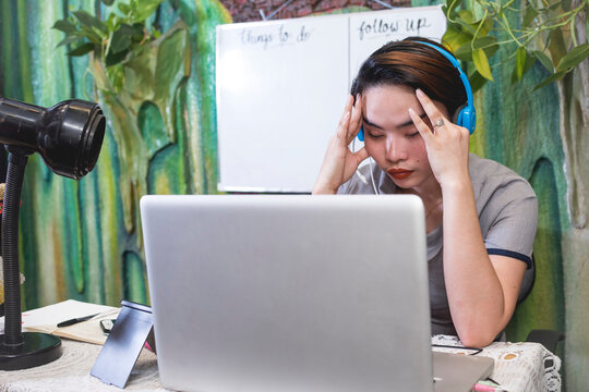 A Young Asian Teacher Is Stressed Out And Massages Her Temple During A Video Conference Or Online Class. Work At Home Concept At Open Air Room.