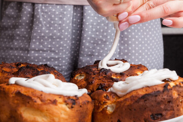 Close-up of decorating freshly baked muffins with white frosting squeezed out of a store tube by female hands with pink nails during a homemade cakes making workshop.