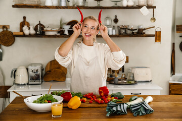 Beautiful happy woman making fun with vegetables while cooking lunch