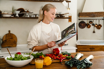 Beautiful joyful woman reading cookbook and smiling while making lunch