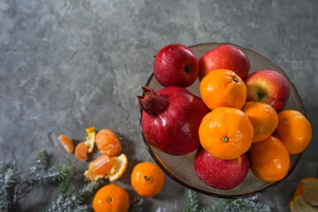 fruits with tangerines in a glass dish on a gray background
