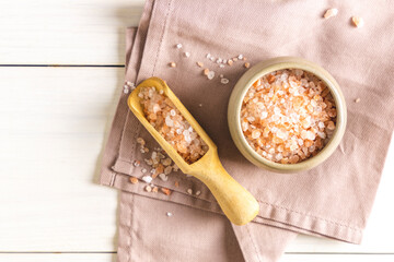 Pink Himalayan rock salt in a ceramic bowl and wooden spoon on a light background