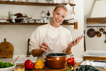 Beautiful woman smiling and using cellphone while making lunch