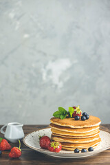 Pancake with strawberry, blueberry and mint in ceramic dish, syrup from small ceramic jar