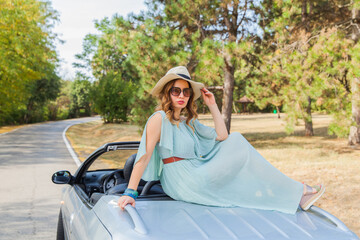 Attractive woman leaning and posing at convertible car. Happy pretty girl. Outdoor fashion portrait