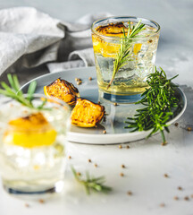 Two glasses of Charred Lemon, Rosemary and Coriander Gin and Tonic is a flavors are perfectly balanced refreshing cocktail. on light background, close up