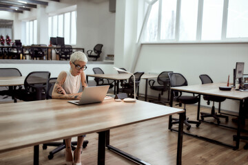 Too much work. Young and busy tattooed businesswoman in eyeglasses working with laptop while...