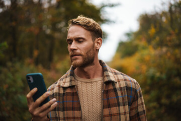 Handsome man using mobile phone while strolling in autumn forest