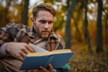 Handsome unshaven man reading book while resting in autumn forest