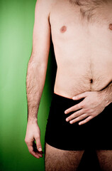 Man holding his hand between belly and crotch. Studio photo isolated on green background.