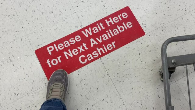 A man patiently waits in a store's check out line while standing on a social distance reminder sticker on the floor. Social distancing was a common sight during the coronavirus pandemic of 2020.	