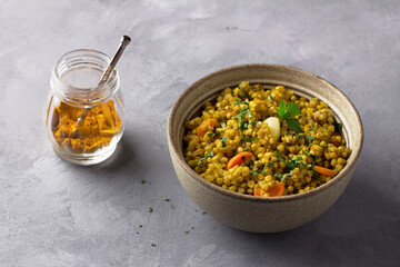 Healthy homemade food bowl with green buckwheat, vegetables (onions, carrots, garlic), greens and curry with glass of water on gray textured background